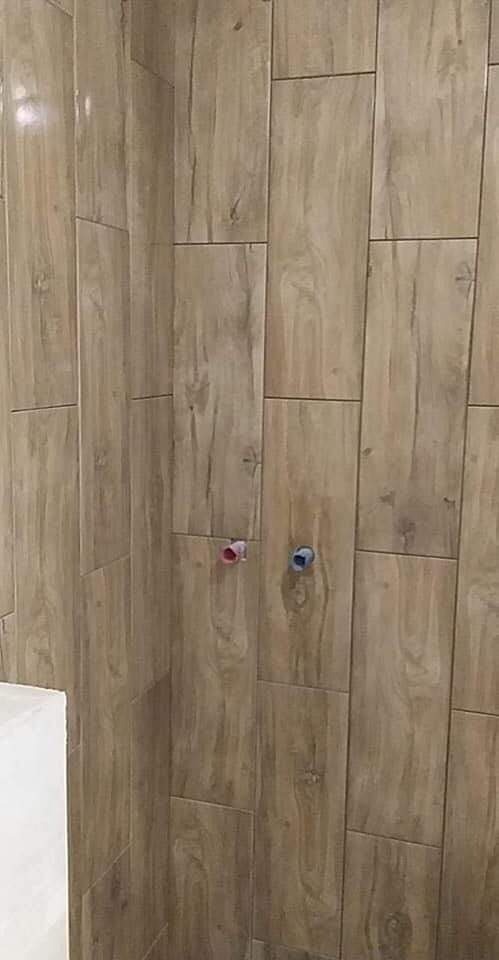 Ściana w łazience wyłożona płytkami ceramicznymi imitującymi drewno, z widocznymi przyłączami wodnymi z zaślepkami w kolorze czerwonym i niebieskim.