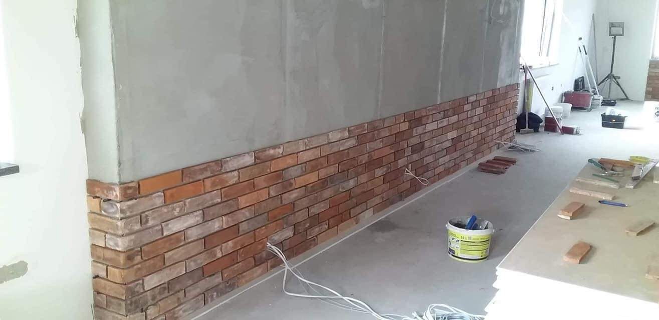 Częściowo wykończona ściana z cegły klinkierowej w pomieszczeniu w Kwidzynie, widoczne narzędzia i materiały budowlane.