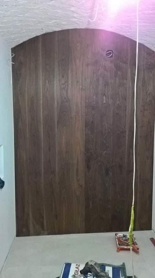 Ściana wykończona panelami drewnopodobnymi w łazience z zaokrąglonym sufitem, widoczne narzędzia glazurnicze i opakowanie po kleju do płytek.