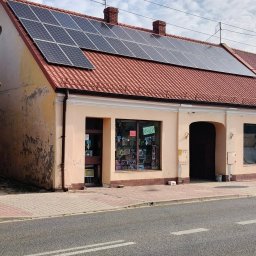 Czyste Elewacje - Budynek z panelami słonecznymi na czerwonym dachu, widoczne ślady zabrudzeń na elewacji. Ujęcie z poziomu ulicy, w tle błękitne niebo z chmurami.