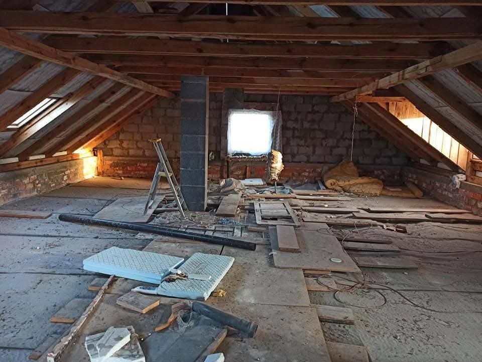 Poddasze w trakcie adaptacji: widoczne krokwie, ceglana ściana, okno z wpadającym światłem, rozłożone materiały izolacyjne i drabina oparta o komin.