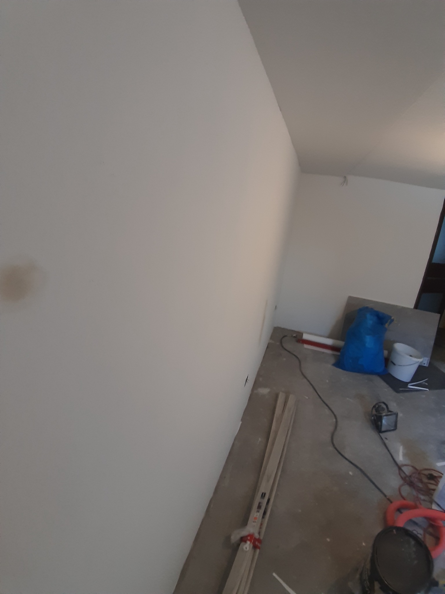 Świeżo pomalowane, białe ściany w pokoju w trakcie remontu, widoczne narzędzia malarskie, listwy przypodłogowe i niebieski worek na gruz.