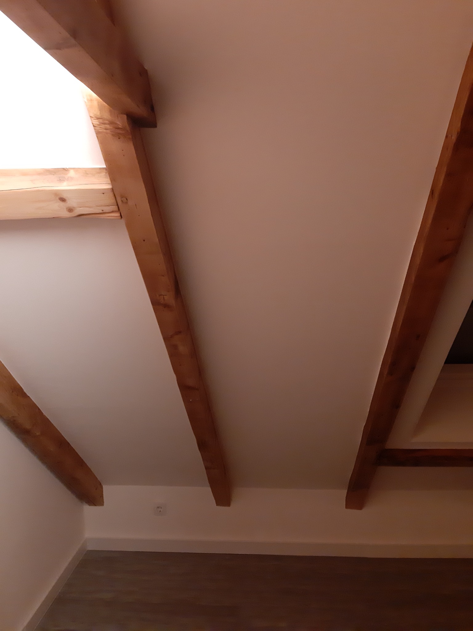 Poddasze po remoncie z widocznymi drewnianymi belkami stropowymi, pomalowanymi ścianami i wykończoną podłogą panelową.