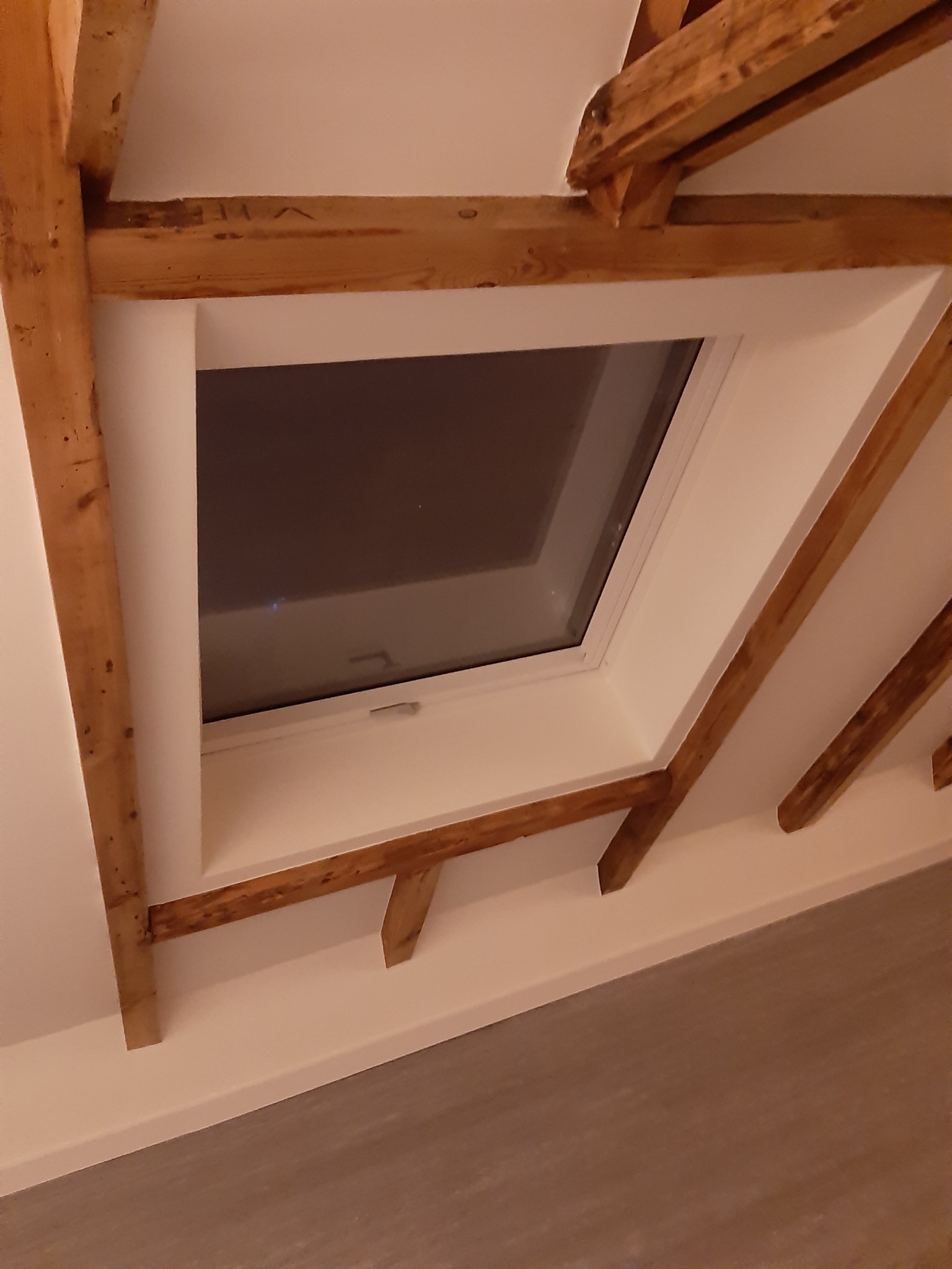 Nowe okno dachowe wkomponowane w drewnianą konstrukcję poddasza, wykończone białą ramą i szpachlowane połączenia z płytą karton gips.