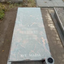 Nowy, granitowy pomnik w Kołobrzegu z wygrawerowanym krzyżem i napisem 'Ave Maria', umieszczony na cmentarzu, z widocznym wazonem na kwiaty.