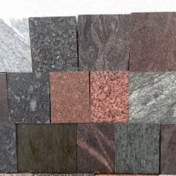 Ekspozycja próbek kwadratowych płyt kamiennych w różnych kolorach i fakturach, ułożonych rzędami, prezentujących szeroki wybór materiałów.