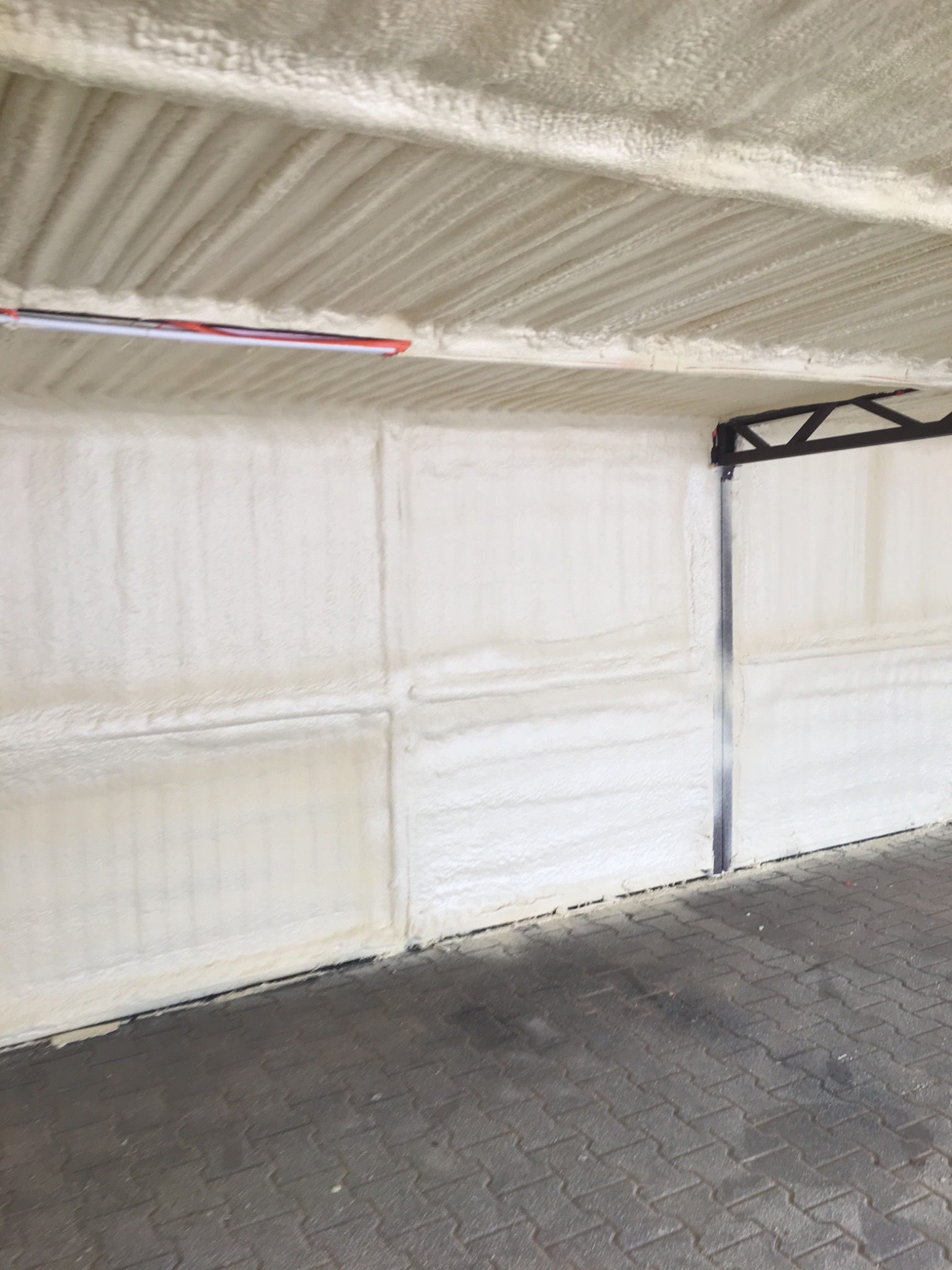 Poddasze garażu po ociepleniu pianką PUR, widoczne równomierne pokrycie ścian i sufitu, szara kostka brukowa na podłodze.