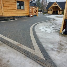 Kiernia AB - Ułożona kostka brukowa w kolorze szarym z jasnymi pasami, tworząca ścieżkę przed drewnianym domem i altaną, z resztkami śniegu na obrzeżach.