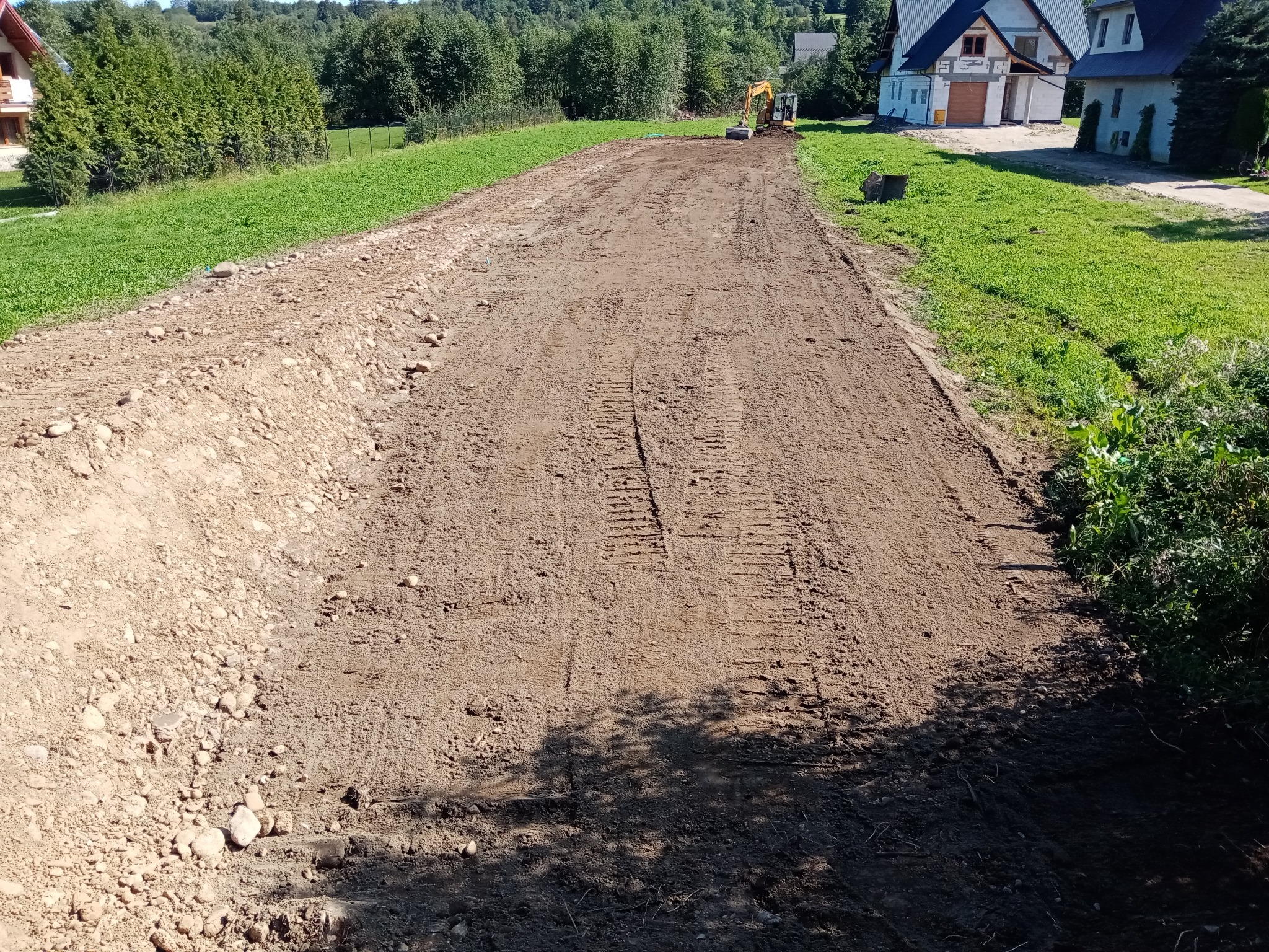 Przygotowany teren pod budowę w Maruszynie, wyrównana ziemia z widocznymi śladami opon i pracującą koparką w oddali.