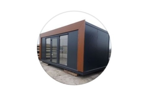 Gotowy modułowy budynek biurowy z ciemnymi panelami i brązowymi ramami okiennymi, widoczne szklane drzwi przesuwne.