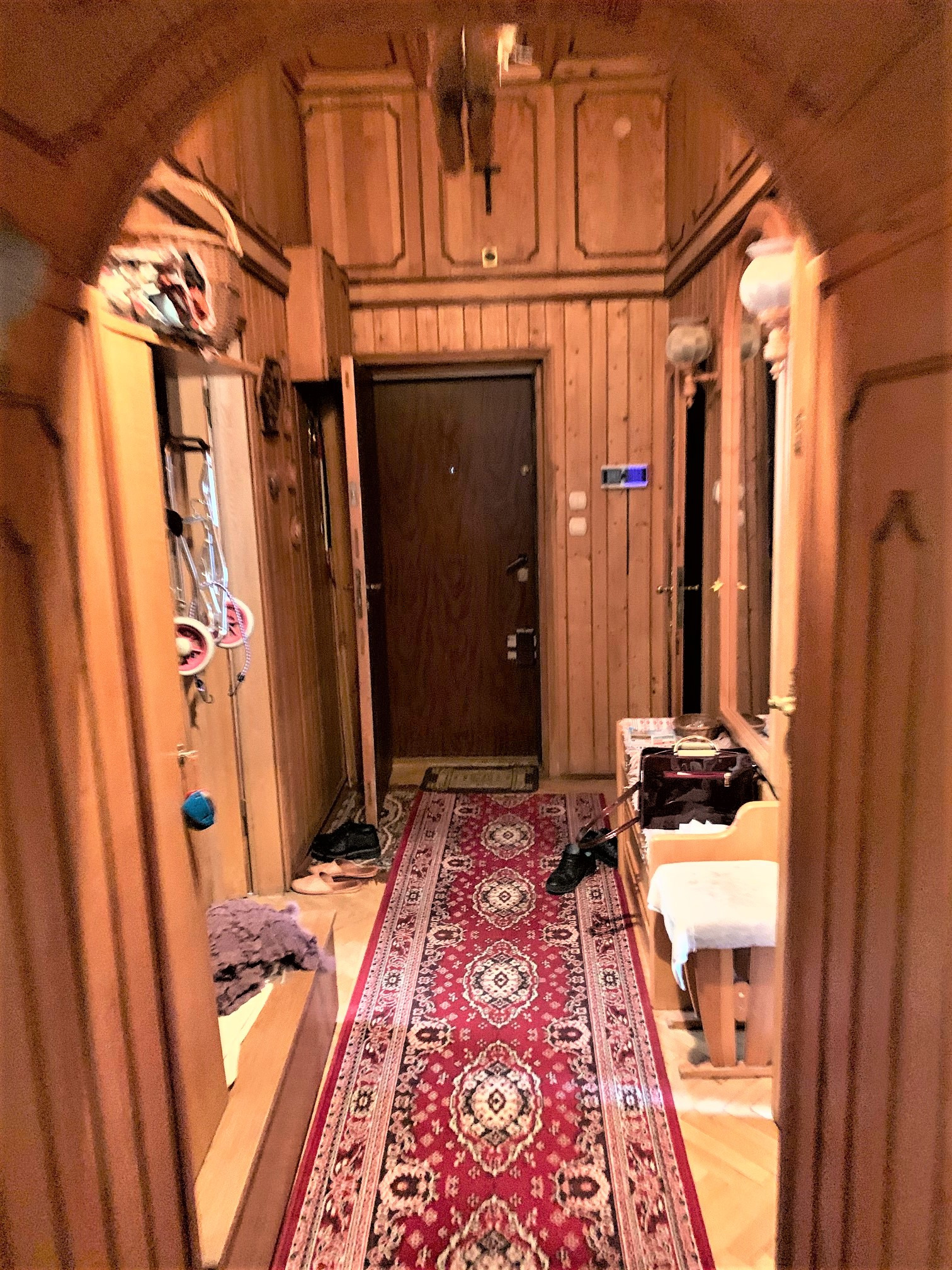 Wnętrze przedpokoju wykończonego drewnianą boazerią z czerwonym dywanem w orientalne wzory, widok na drzwi wejściowe.