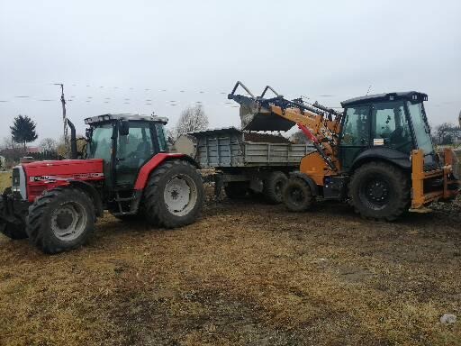 Czerwony traktor i żółto-czarna koparko-ładowarka w trakcie załadunku ziemi na przyczepę w pochmurny dzień.