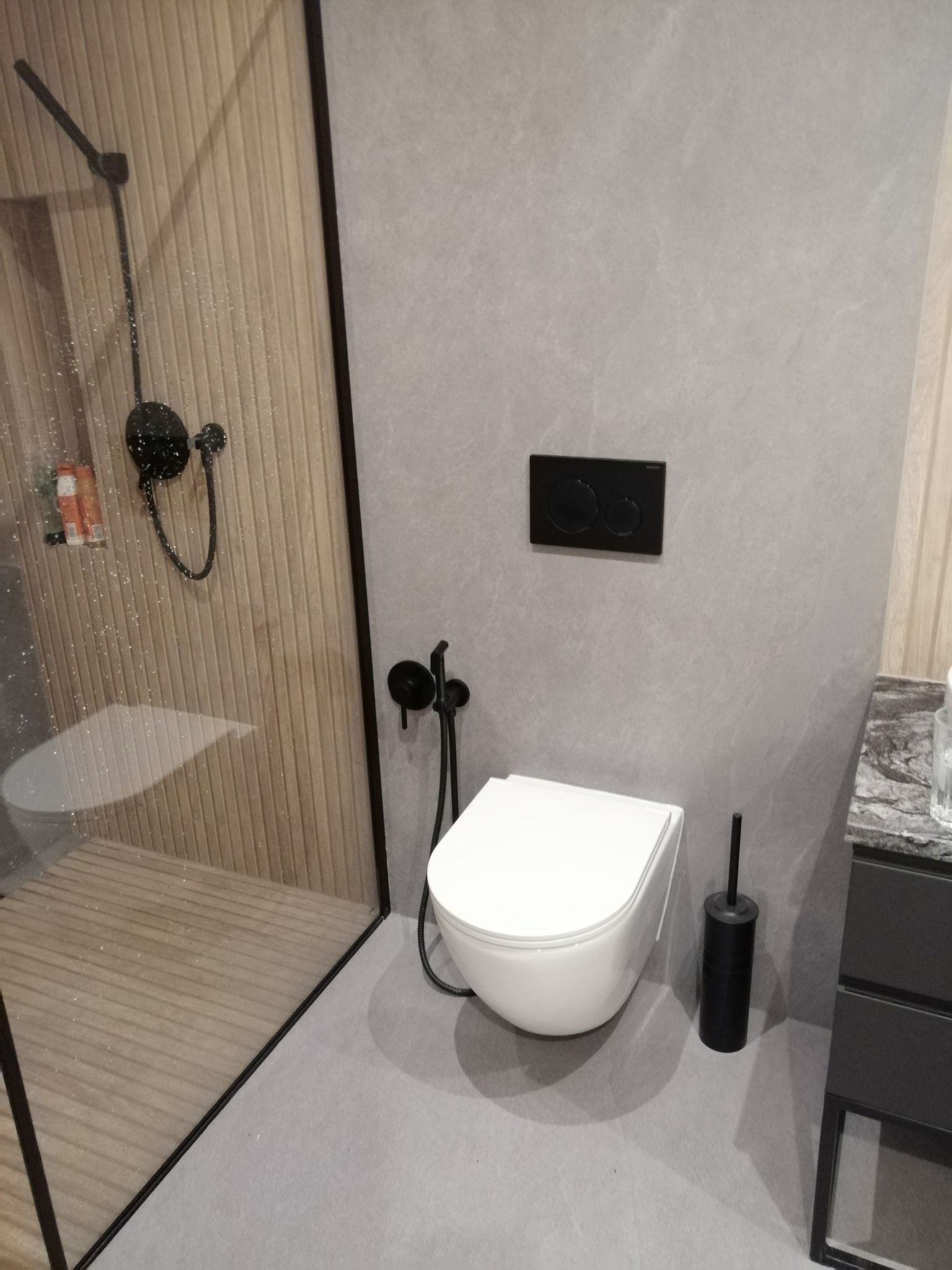 Nowoczesna łazienka z kabiną prysznicową ze szklaną ścianką z drewnianymi panelami, wiszącą toaletą i czarną armaturą.