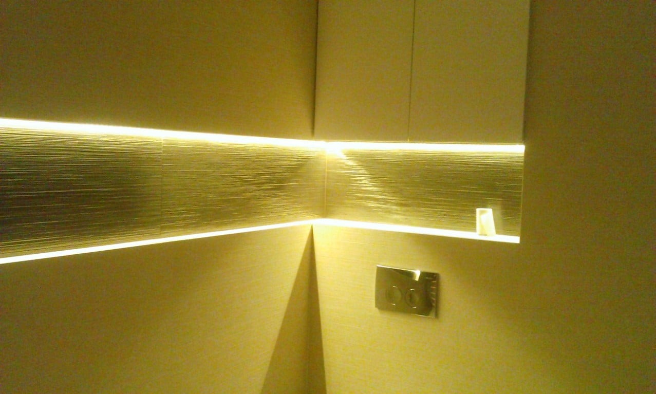 Ściana wykończona dekoracyjnym panelem z poziomymi żłobieniami, oświetlona listwą LED, z widocznym włącznikiem światła.