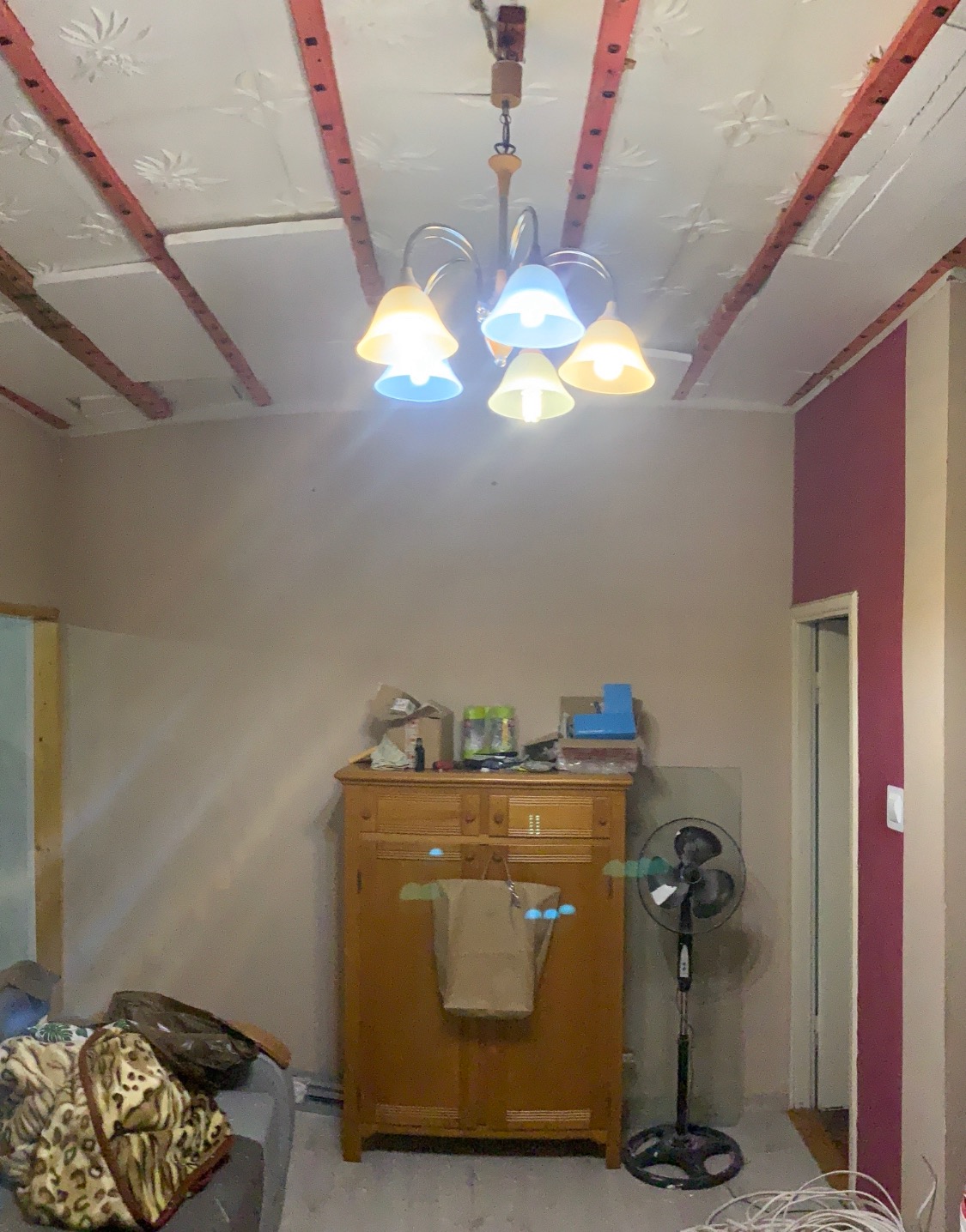 Pokój w trakcie prac: widoczne fragmenty sufitu z dekoracyjnym wzorem, częściowo ocieplone wełną mineralną, stara szafa z workiem i wentylator pokojowy.