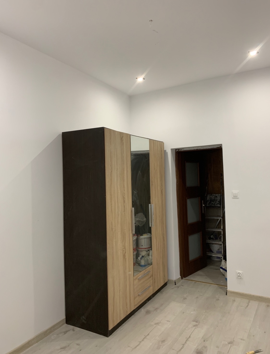 Montaż szafy przesuwnej z lustrem w nowym mieszkaniu, widok na częściowo wykończone wnętrze z drewnianą podłogą i otwartymi drzwiami do garderoby.
