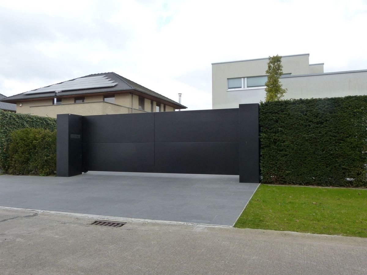 Nowoczesna, przesuwna brama wjazdowa w kolorze antracytu, zintegrowana ze słupkami i nawierzchnią z szarej kostki, otoczona zielenią.