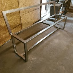 Kanak Welder - Surowy, spawany szkielet metalowej ławki, widoczny w warsztacie na tle ściany z płyt OSB i sprzętu spawalniczego.