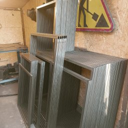 Kanak Welder - Stos metalowych ram z profili kwadratowych, przygotowanych do dalszej obróbki, w tle płyta OSB i znak drogowy ostrzegający o robotach.