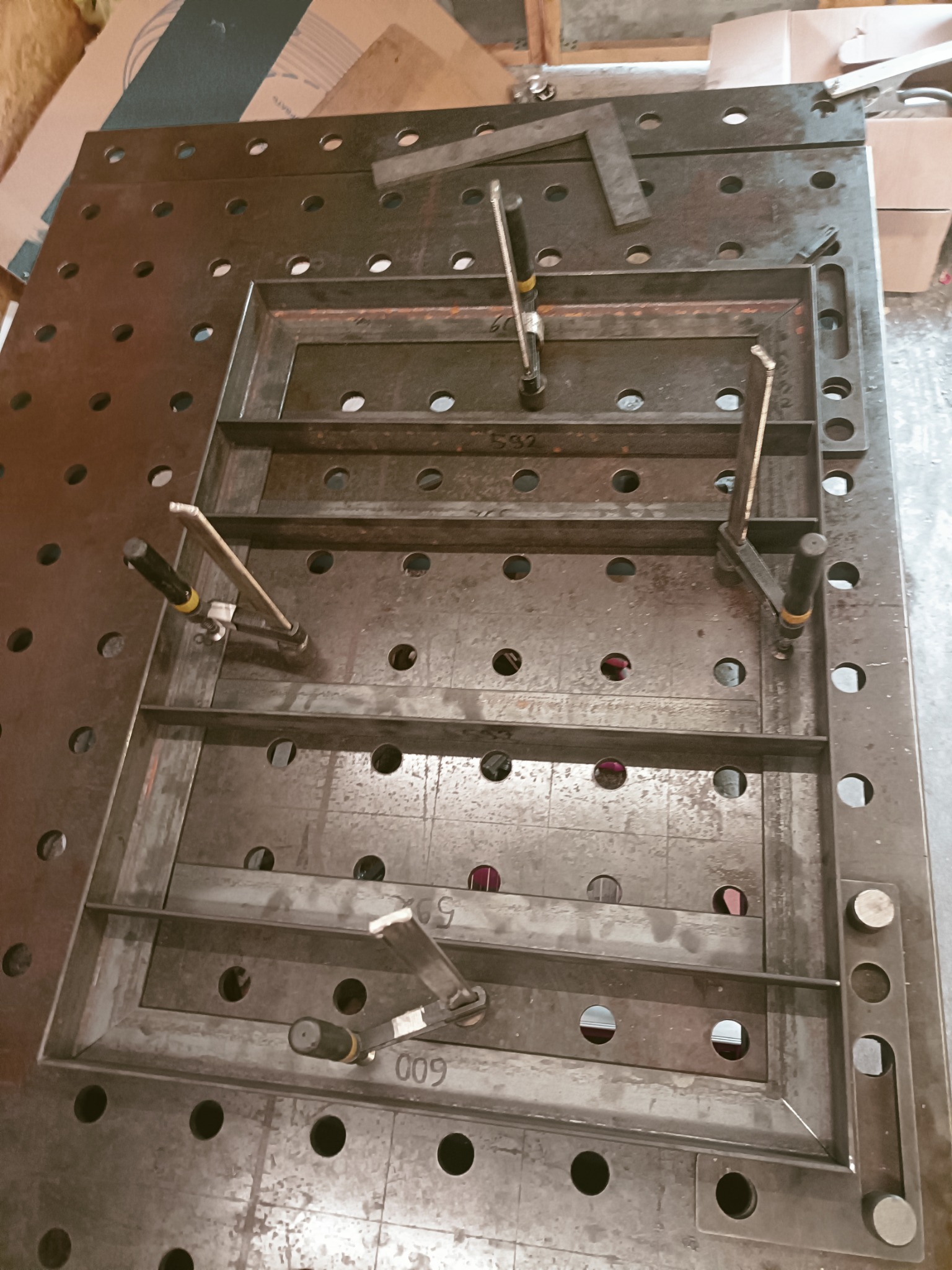 Metalowa konstrukcja ramy z poprzeczkami, zamocowana klamrami na perforowanym stole spawalniczym w Otwocku, widok z góry.