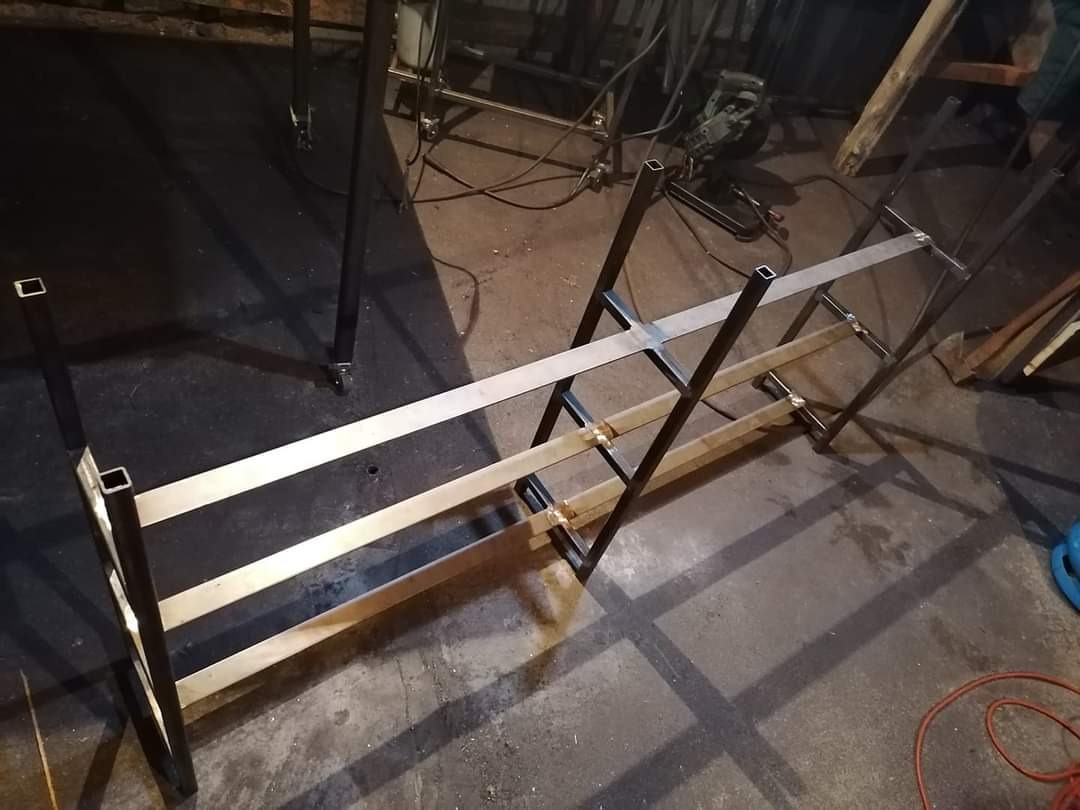 Metalowa konstrukcja w trakcie spawania, widoczne profile kwadratowe i płaskowniki, surowy warsztat.