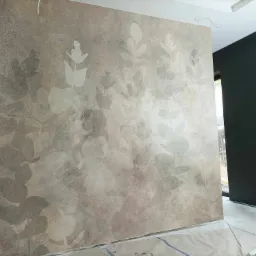 Ściana w pokoju po malowaniu z efektem dekoracyjnym liści, zabezpieczona folią podłoga, widoczne gniazdko elektryczne.