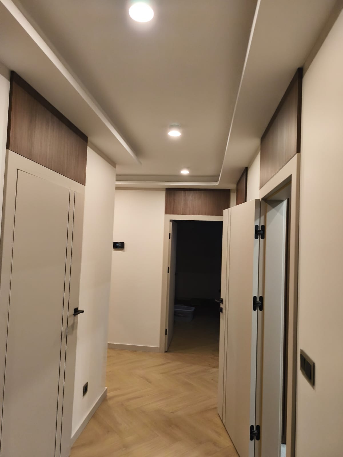 Nowoczesny korytarz po remoncie w Szczucinie. Jasne ściany, drewniane akcenty na suficie i drzwiach, parkiet w jodełkę. Widoczne oświetlenie punktowe i minimalistyczne wykończenie.