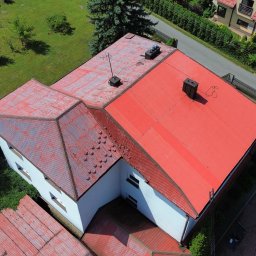 Dach-Mal Jarosław Zięba - Czerwony dach domu z blachy trapezowej, widok z lotu ptaka. Część dachu pomalowana, część z widocznymi śladami korozji. Kominy i anteny na dachu. Otoczenie: zieleń, zabudowa jednorodzinna.