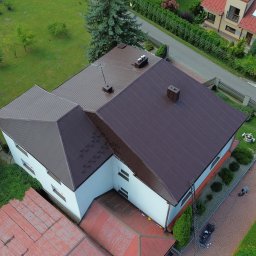 Dach-Mal Jarosław Zięba - Zdjęcie z drona przedstawia dom z brązowym dachem z blachy trapezowej, białą elewacją i zielonym otoczeniem. Widoczny komin, drzewa i fragment ulicy.
