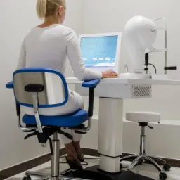 Pacjentka siedzi tyłem na krześle Schwind przed urządzeniem diagnostycznym Schwind Sirius w gabinecie.