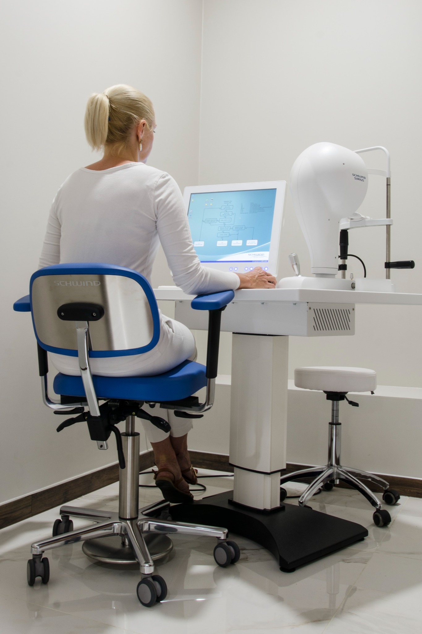 Pacjentka siedzi tyłem na krześle Schwind przed urządzeniem diagnostycznym Schwind Sirius w gabinecie.