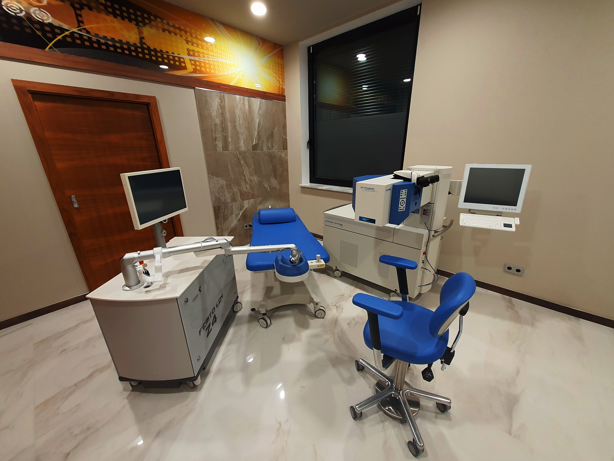 Kadr z gabinetu okulistycznego z laserem Femto LDV Z4, fotelem pacjenta w kolorze niebieskim i sprzętem diagnostycznym na błyszczącej marmurowej podłodze.