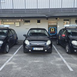 Omega Balcerak Sp. z o.o. - Trzy czarne samochody z napisem 'Ochrona' na dachu zaparkowane przed budynkiem z logo firmy ochroniarskiej 'Balcerak'.