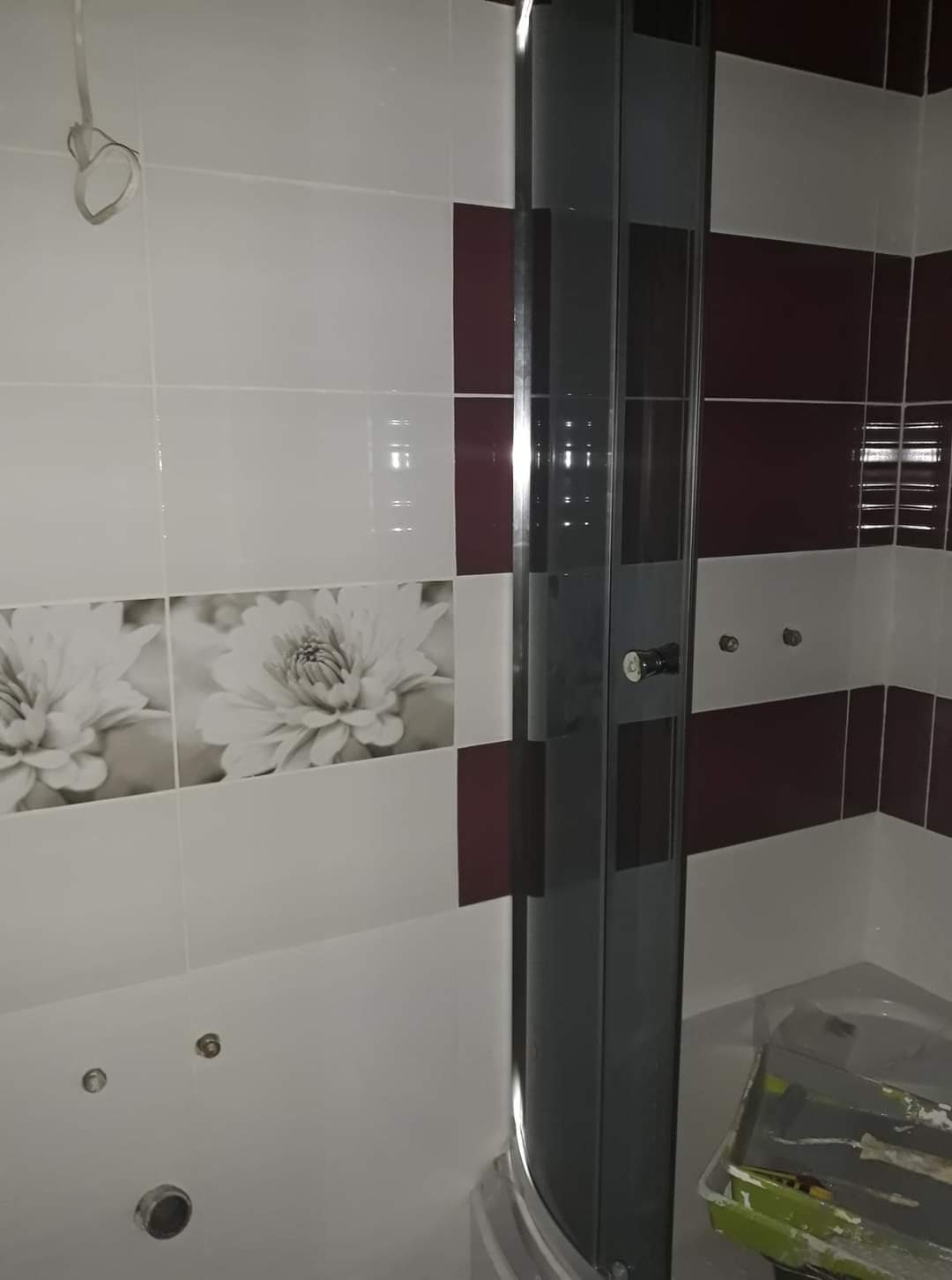 Wykończona łazienka z kabiną prysznicową, biało-bordowe płytki z motywem kwiatowym, widoczna farba w kuwecie malarskiej sugerująca trwające prace wykończeniowe.