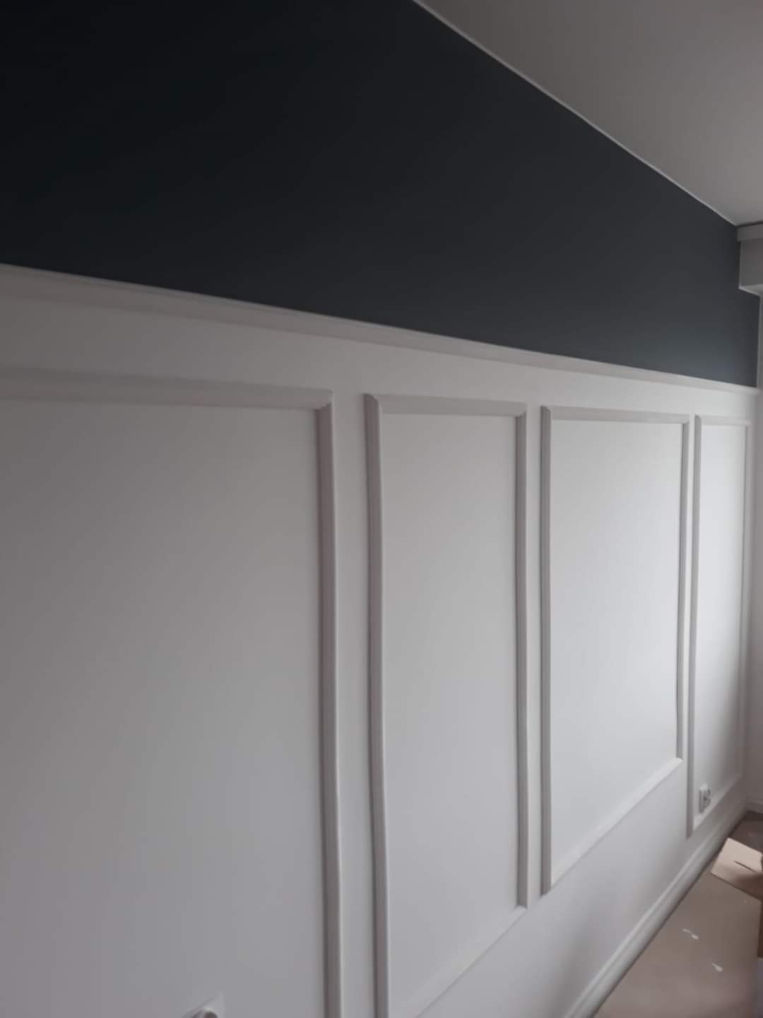 Ściana z białymi panelami dekoracyjnymi i ciemnoszarą górną częścią, widok z boku, minimalistyczny design.