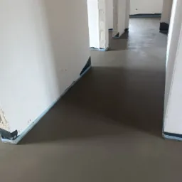 Świeżo wylana, gładka posadzka w surowym stanie, z widocznymi dylatacjami przy ścianach, przygotowana do dalszych prac wykończeniowych.