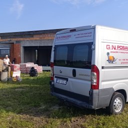 GŁOWSKI NIEDZIELSKI SPÓŁKA CYWILNA - Ekipa przy pracy: maszyna do jastrychu, worki i bus firmy G.N. Posadzki na tle budowy. Widoczni pracownicy przygotowujący mieszankę. Dzień słoneczny.