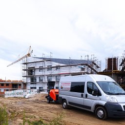 GŁOWSKI NIEDZIELSKI SPÓŁKA CYWILNA - Srebrny bus z logo firmy G.N. Posadzki na tle budowy i pompy do jastrychu. Widoczny dźwig i rusztowania. Maszynowe posadzki Gniezno.