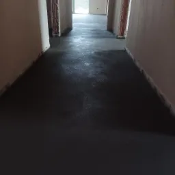 Świeżo wylana, mokra, ciemna wylewka podłogowa w korytarzu budynku w stanie surowym, widoczne ślady po narzędziach.