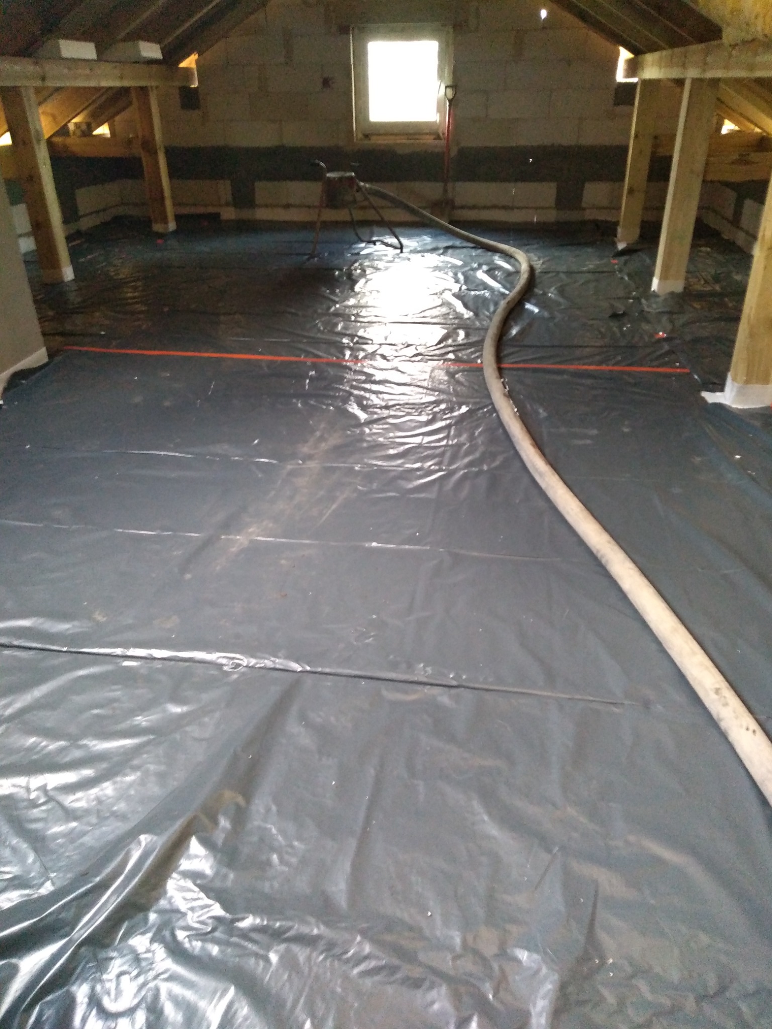 Przygotowanie podłoża pod wylewkę na poddaszu: folia ochronna rozłożona na podłodze, widoczny wąż do wylewki i konstrukcja więźby dachowej.