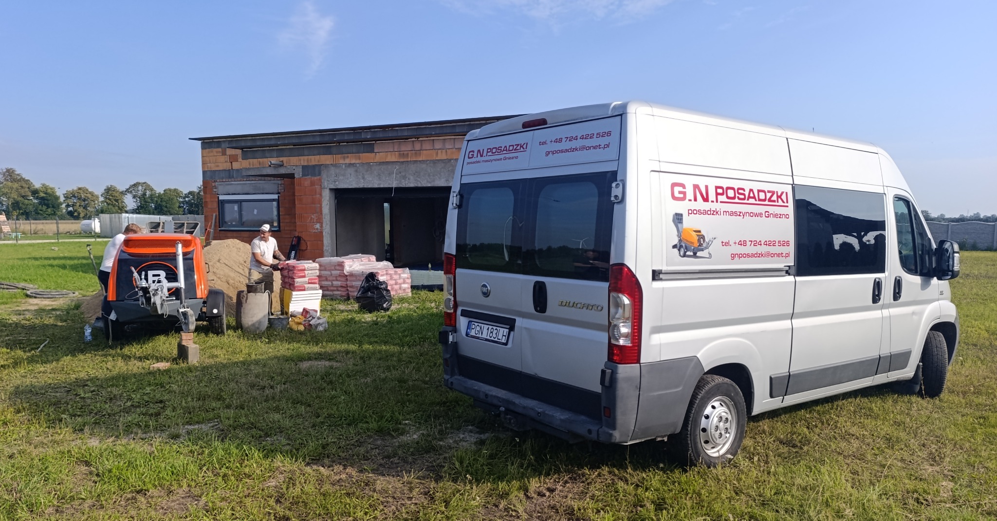 Ekipa przy pracy: maszyna do jastrychu, worki i bus firmy G.N. Posadzki na tle budowy. Widoczni pracownicy przygotowujący mieszankę. Dzień słoneczny.