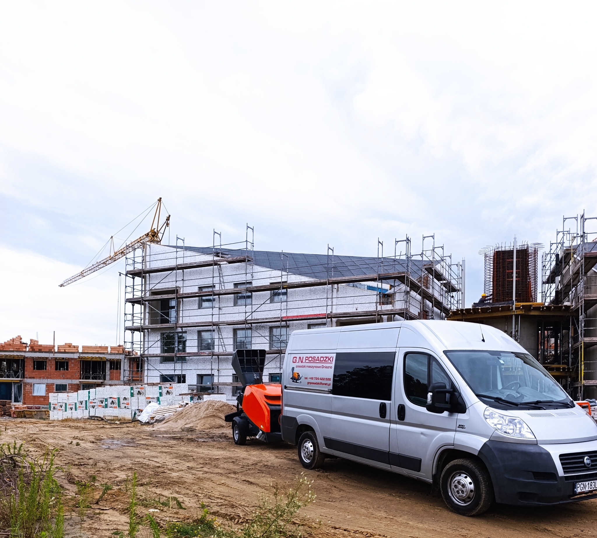 Srebrny bus z logo firmy G.N. Posadzki na tle budowy i pompy do jastrychu. Widoczny dźwig i rusztowania. Maszynowe posadzki Gniezno.