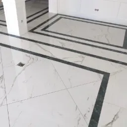 Biała marmurowa podłoga z ciemnoszarymi akcentami w eleganckim wnętrzu, widoczny fragment kolumny i listwy przypodłogowe.