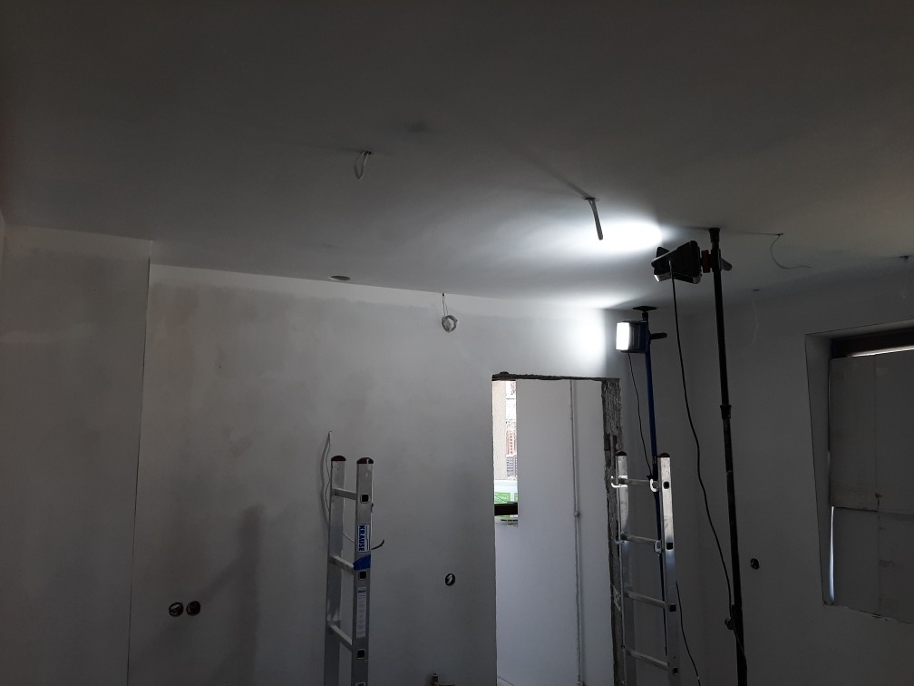 Wnętrze w trakcie prac wykończeniowych: szpachlowane ściany, drabina Krause i lampa halogenowa oświetlająca sufit.