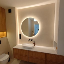 Mikrocement Podlasie - Nowoczesna łazienka z okrągłym lustrem LED, drewnianą szafką pod umywalką i beżową, jednolitą powierzchnią ścian. Minimalistyczny design.