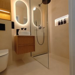 Mikrocement Podlasie - Elegancka łazienka z beżową posadzką żywiczną, kabiną prysznicową ze szklaną ścianą i oświetlonymi lustrami. Minimalistyczny design, nowoczesne wykończenie.