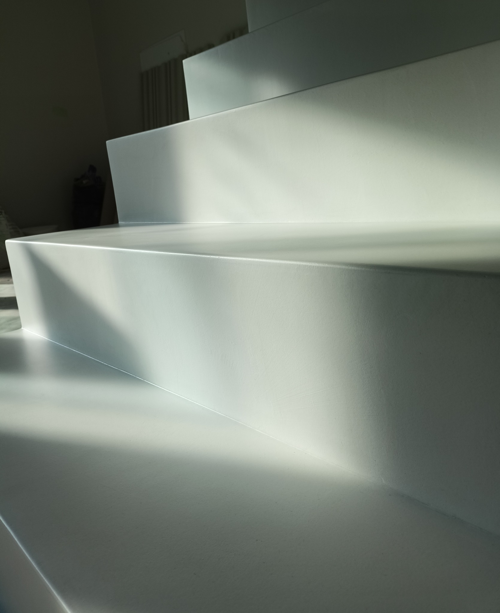 Nowoczesne, minimalistyczne schody o jednolitej, białej powierzchni, oświetlone naturalnym światłem tworzącym dynamiczne cienie.