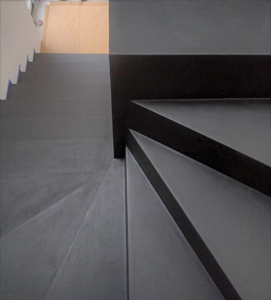 Stylowe schody z szarą, gładką powierzchnią, wykończone czarną balustradą. Widok z góry ukazuje minimalistyczny design i nowoczesne wykończenie.