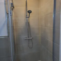 Nowoczesna kabina prysznicowa z deszczownicą i szklanymi drzwiami, wyłożona beżowymi płytkami w łazience.