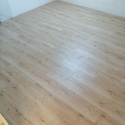 DF usługi remontowe Dawid Fyda - Ukończona podłoga z płytek imitujących drewno ułożonych w prostym wzorze, jasne ściany w tle.